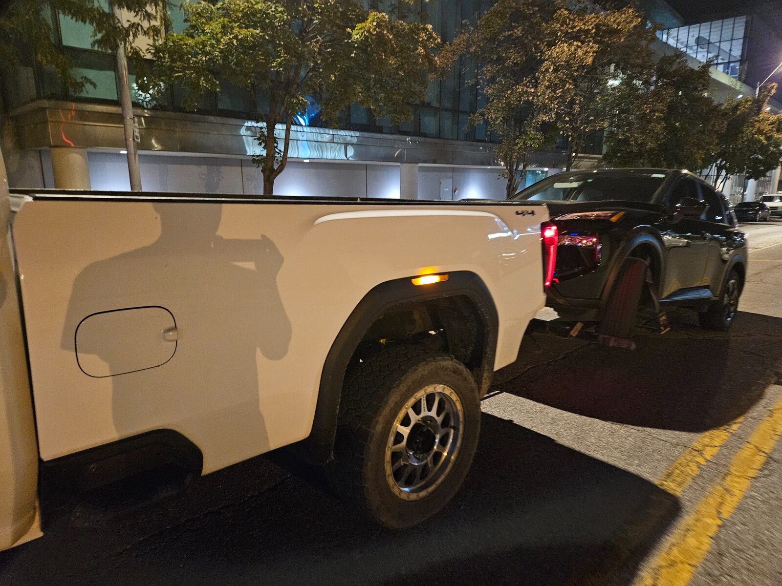 White wheel-lift truck transporting a dark SUV at night on McGee Street in Kansas City.